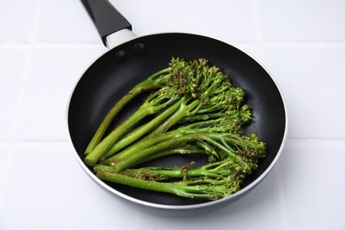 Photo of Frying pan with tasty cooked broccolini on white tiled table