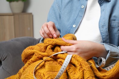 Photo of Woman sewing sweater with needle at home, closeup