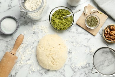 Making delicious pesto bread. Raw dough and ingredients on white marble table, flat lay