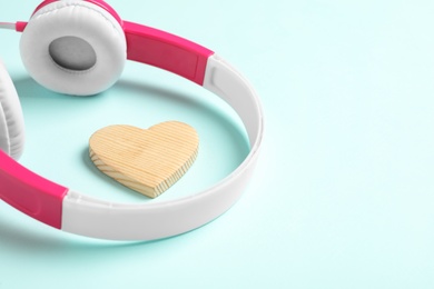 Photo of Modern headphones and wooden heart on turquoise background, space for text. Listening love music songs