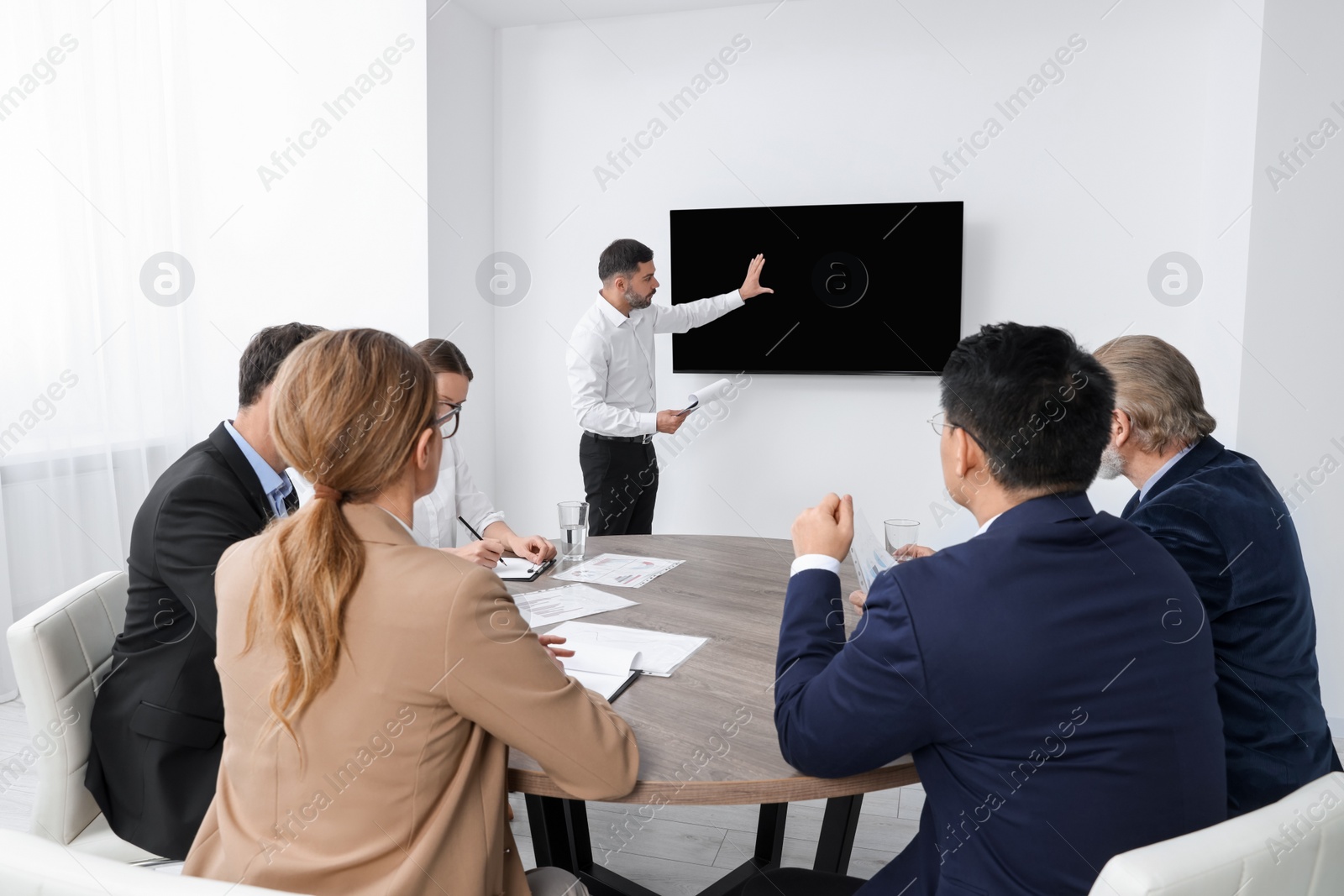 Photo of Business conference. Group of people listening to speaker report near tv screen in meeting room