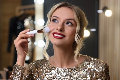 Photo of Beautiful makeup. Smiling woman applying powder with brush onto face in dressing room