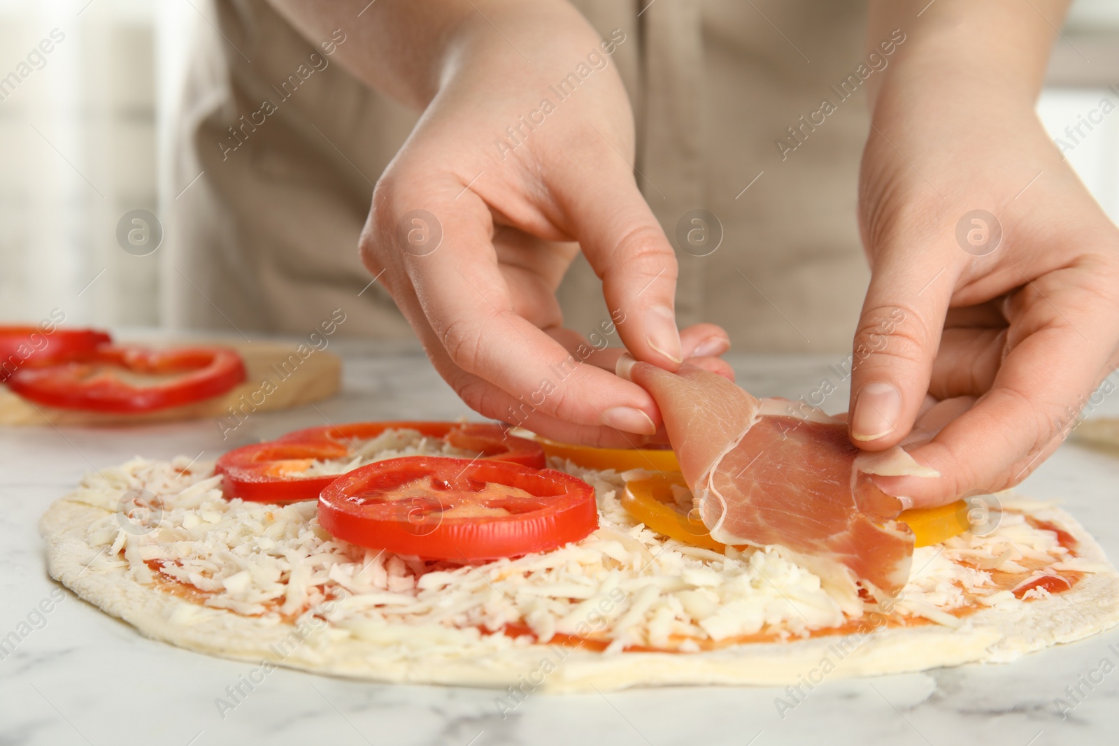 Photo of Woman adding prosciutto to pizza white marble table, closeup