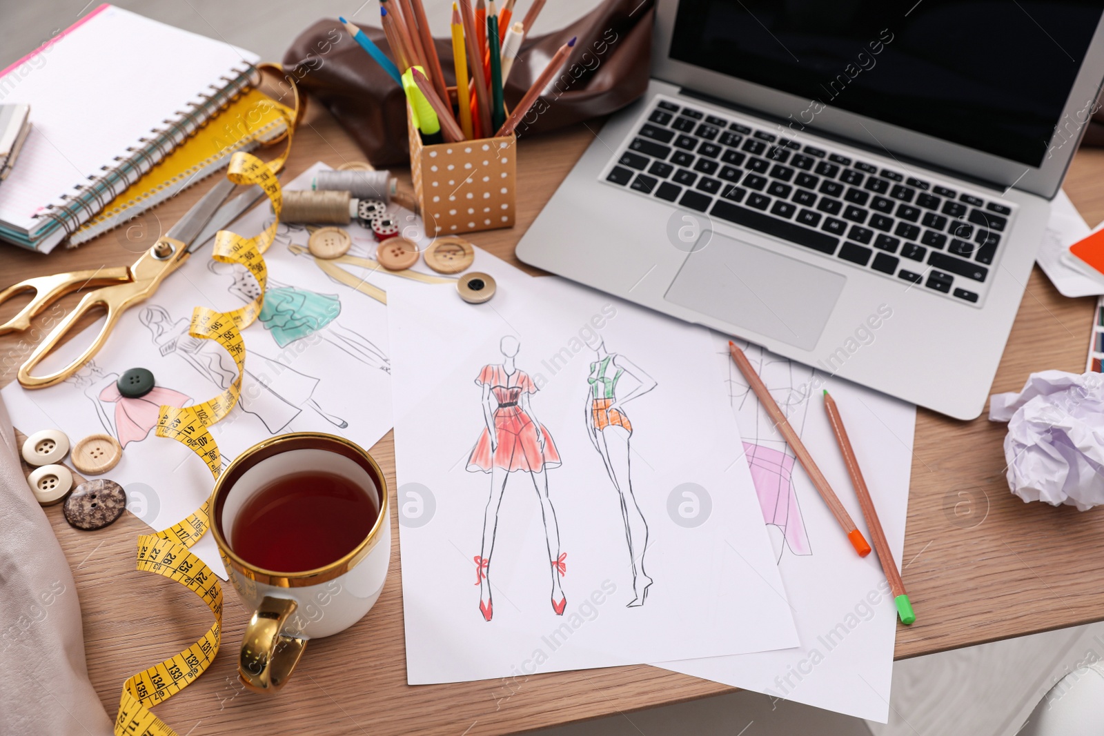 Photo of Sketches of clothes and different stuff on wooden table. Fashion designer's workplace