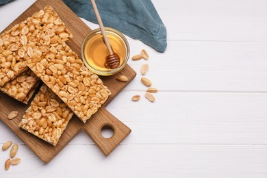 Photo of Tasty kozinaki bars, peanuts and honey on white wooden table, flat lay. Space for text