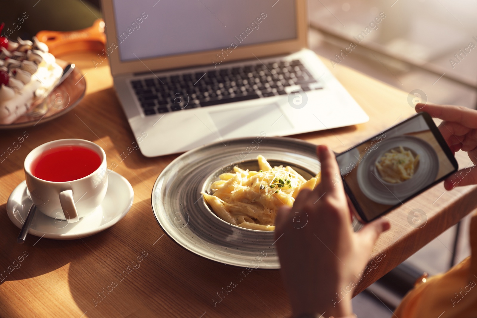 Photo of Young blogger taking picture of pasta at table in cafe, closeup