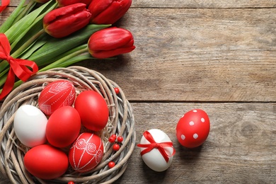 Photo of Flat lay composition of nest with painted Easter eggs and flowers on wooden table, space for text