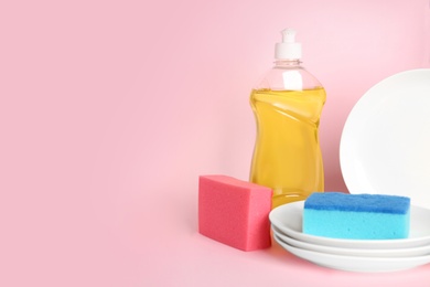 Detergent, plates and sponges on pink background, space for text. Clean dishes