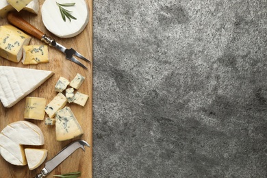 Photo of Cheese platter with specialized knife and fork on grey table, flat lay. Space for text