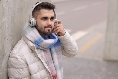 Photo of Handsome man in warm scarf and headphones on city street. Space for text
