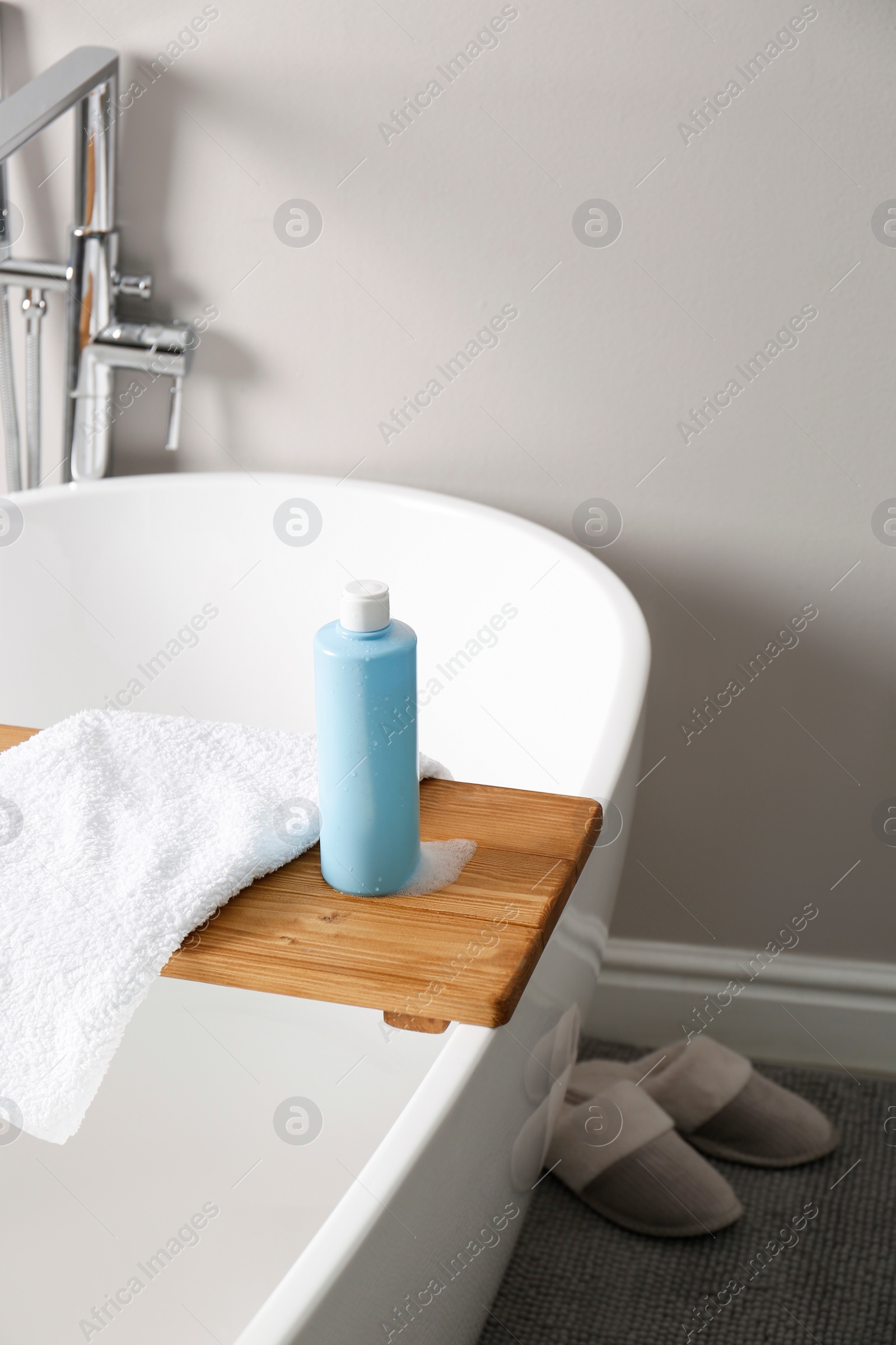 Photo of Bottle of bubble bath with foam and towel on tub in bathroom