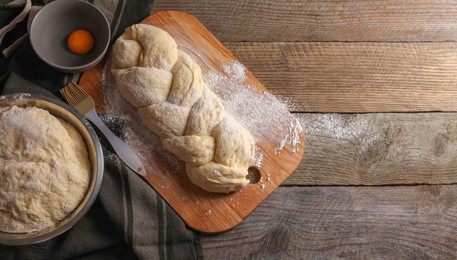 Photo of Homemade braided bread and ingredients on wooden table, flat lay with space for text. Cooking traditional Shabbat challah