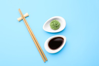 Photo of Swirl of wasabi paste, soy sauce and chopsticks on light blue background, flat lay