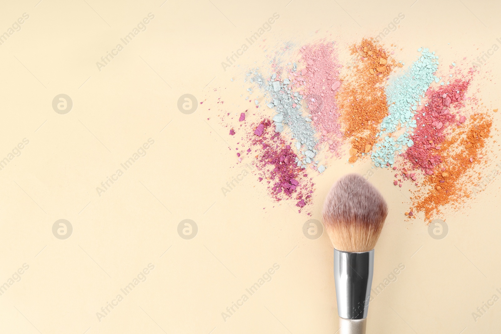 Photo of Makeup brush and scattered eye shadows on beige background, flat lay. Space for text