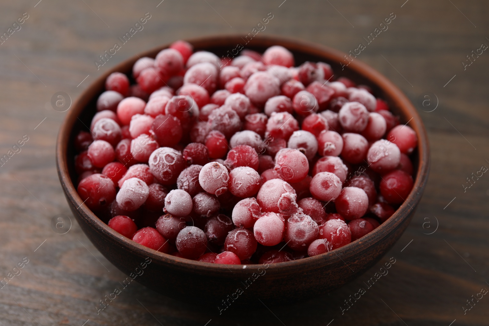 Photo of Frozen red cranberries in bowl on wooden table, closeup