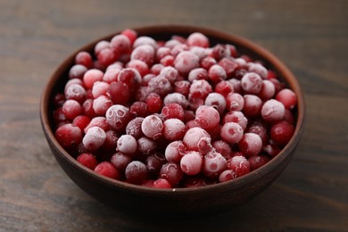 Frozen red cranberries in bowl on wooden table, closeup