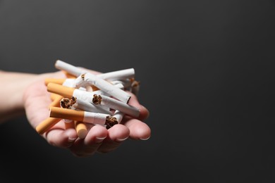 Stop smoking. Woman holding broken cigarettes on black background, closeup. Space for text