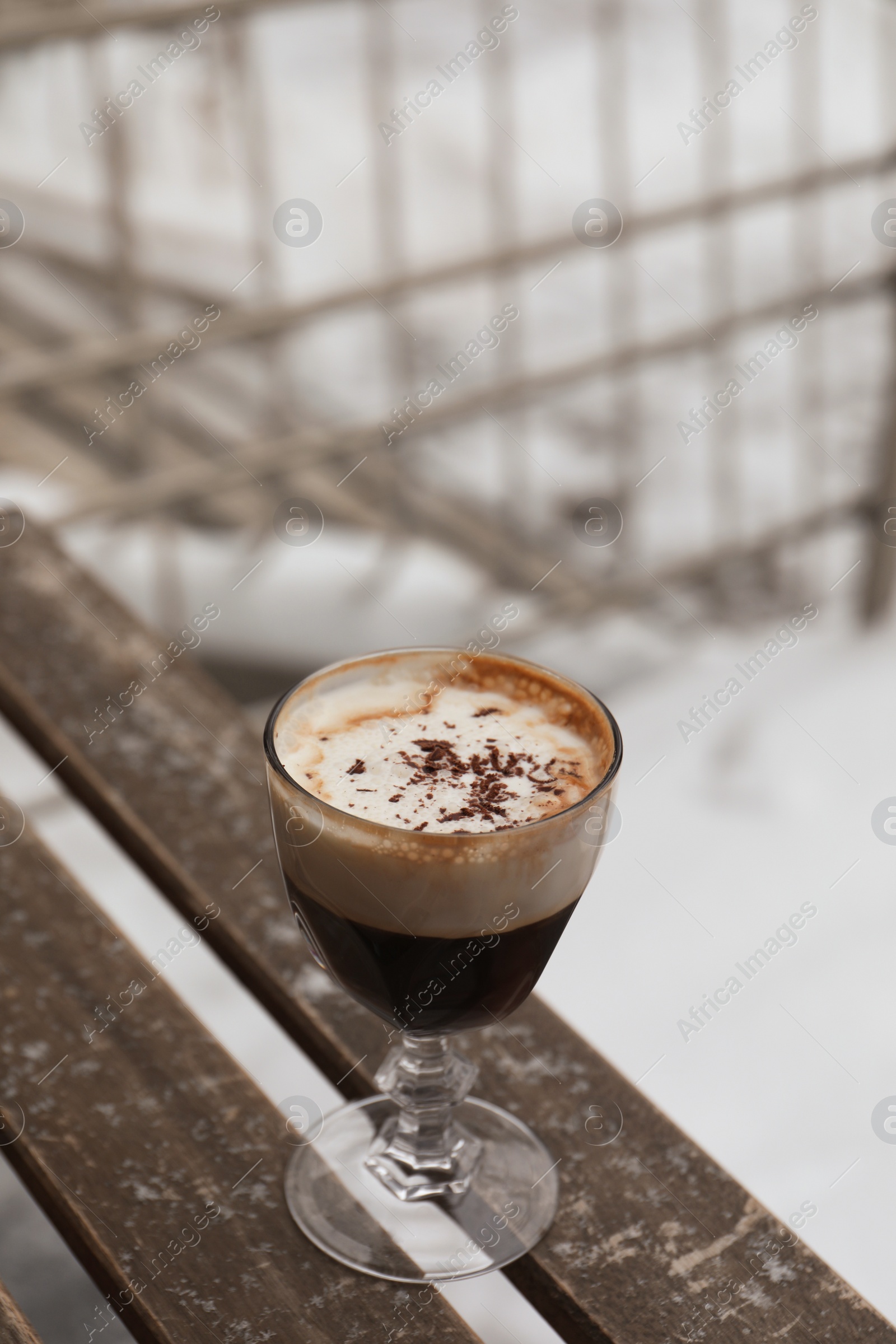 Photo of Glass of aromatic coffee with chocolate powder on wooden bench outdoors in winter