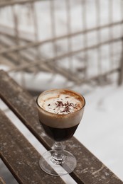 Photo of Glass of aromatic coffee with chocolate powder on wooden bench outdoors in winter