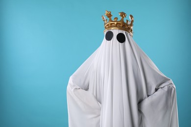 Photo of Person in ghost costume and luxurious crown on light blue background, space for text