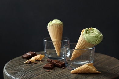 Photo of Delicious pistachio ice cream in wafer cones and chocolate pieces on wooden table. Space for text