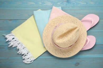 Photo of Beach towel, straw hat and flip flops on light blue wooden background, flat lay