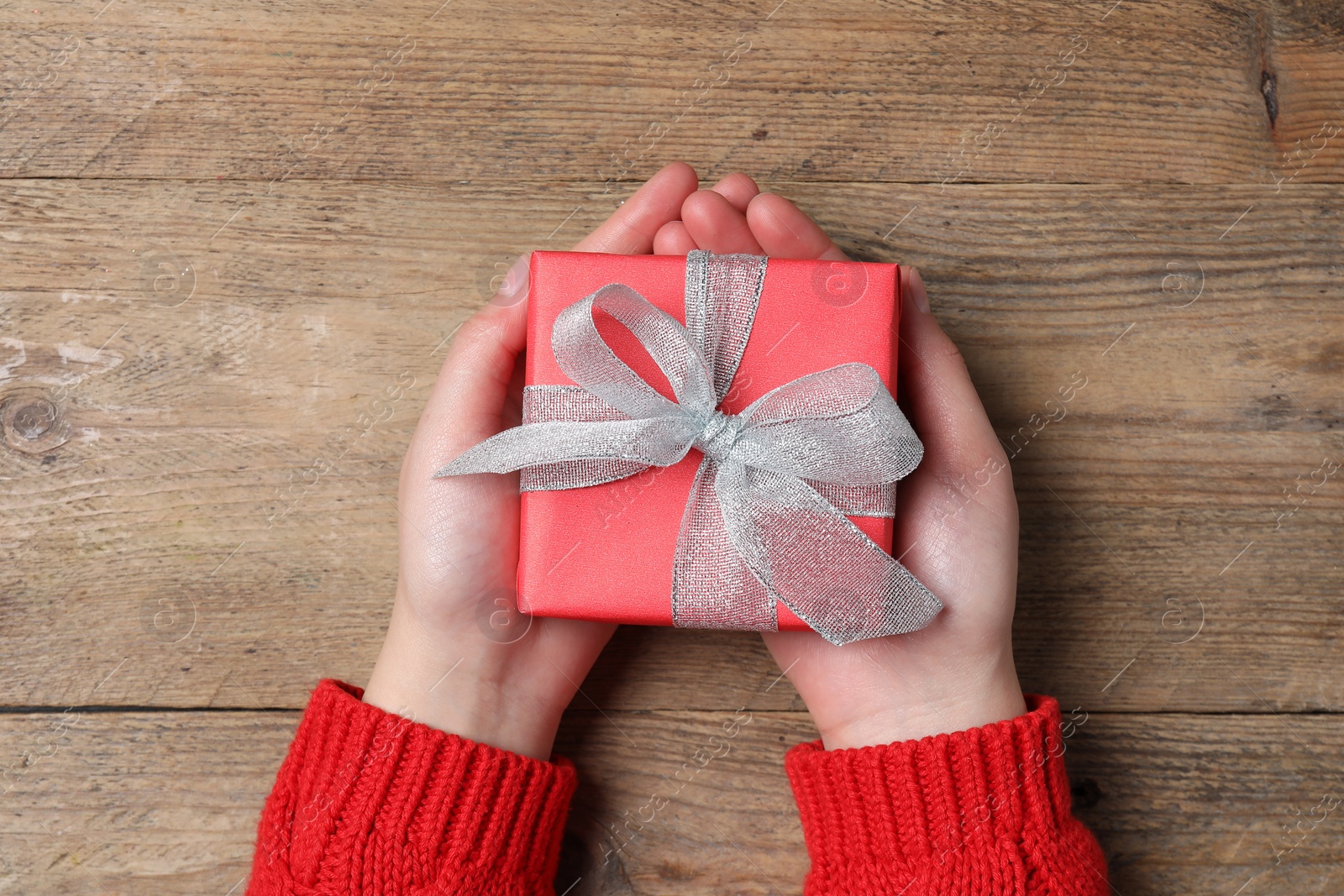 Photo of Christmas present. Woman holding gift box at wooden table, top view