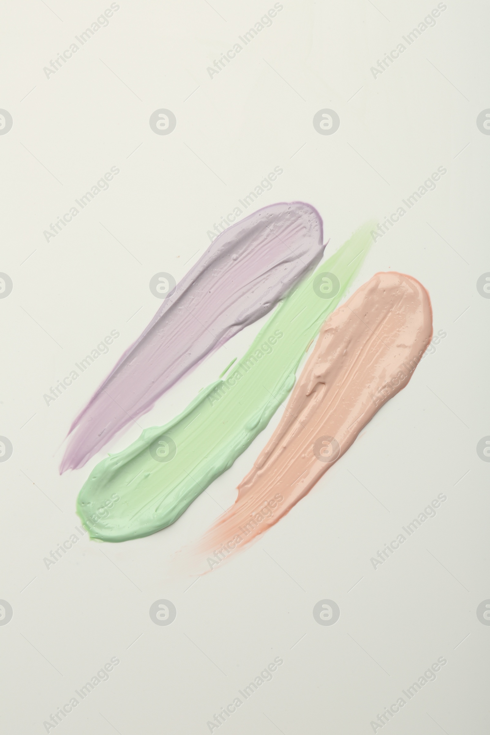 Photo of Strokes of pink, green and purple color correcting concealers on white background, top view