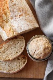 Sourdough starter in glass jar and bread on wooden table, top view