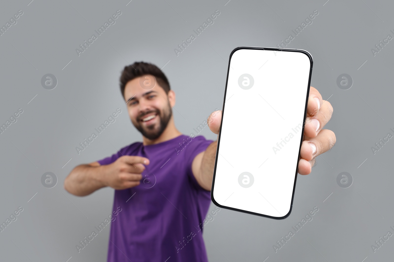 Photo of Young man showing smartphone in hand and pointing at it on light grey background, selective focus. Mockup for design