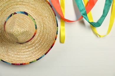 Photo of Mexican sombrero hat and colorful ribbons on white wooden background. Space for text