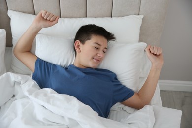 Cute teenage boy stretching in bed at home