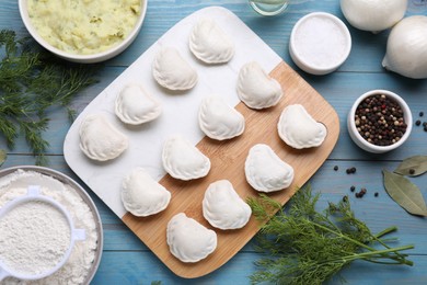 Raw dumplings (varenyky) and ingredients on light blue table, flat lay