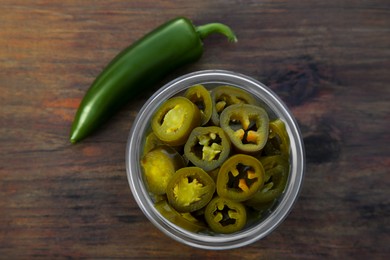 Photo of Fresh and pickled green jalapeno peppers on wooden table, flat lay