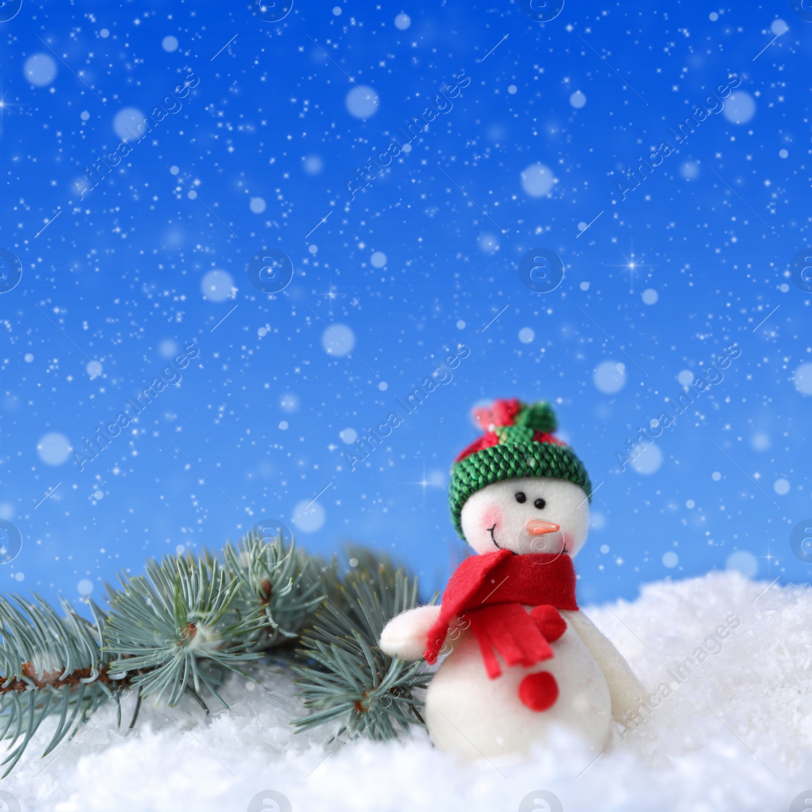 Image of Cute snowman and fir tree branch on snow against blue background, bokeh effect