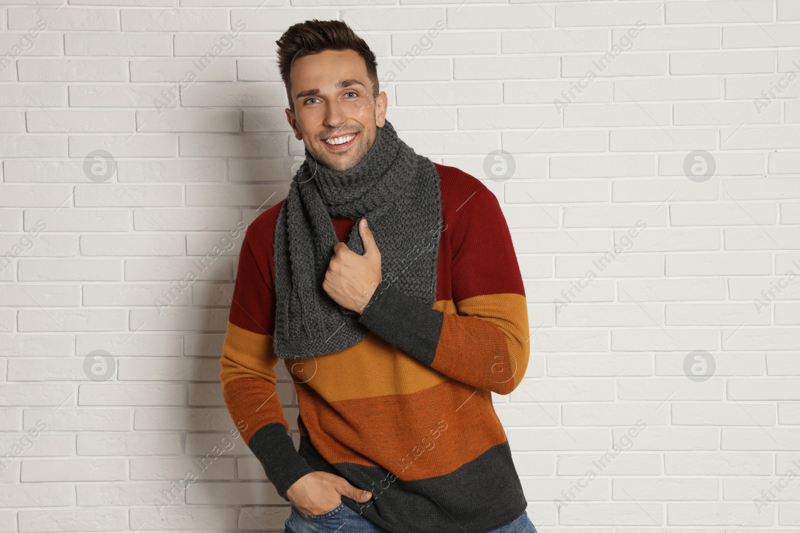 Photo of Happy young man in scarf and warm sweater near white brick wall. Winter season