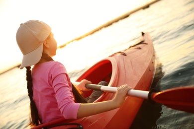 Photo of Little girl kayaking on river at sunset. Summer camp activity