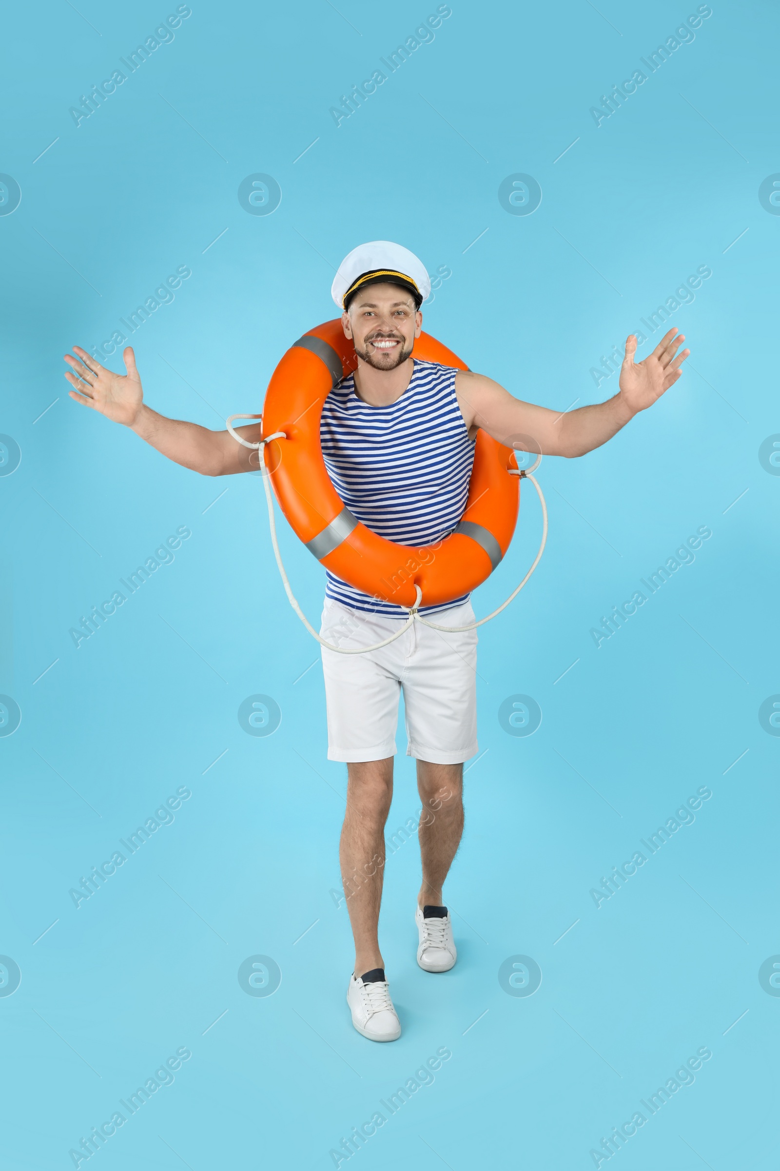 Photo of Happy sailor with orange ring buoy on light blue background