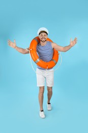 Photo of Happy sailor with orange ring buoy on light blue background