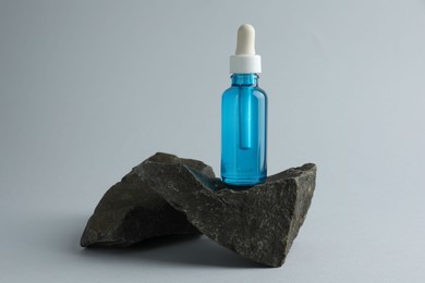 Photo of Bottle of cosmetic serum on stone against light grey background