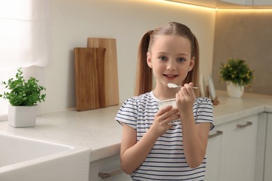 Cute little girl with tasty yogurt in kitchen