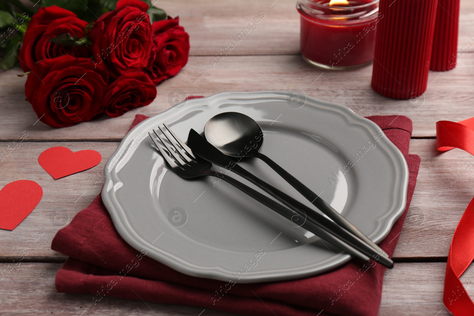 Photo of Romantic place setting with red roses and candle on wooden table. St. Valentine's day dinner