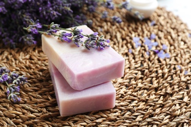 Photo of Handmade soap bars with lavender flowers on wicker mat, closeup. Space for text