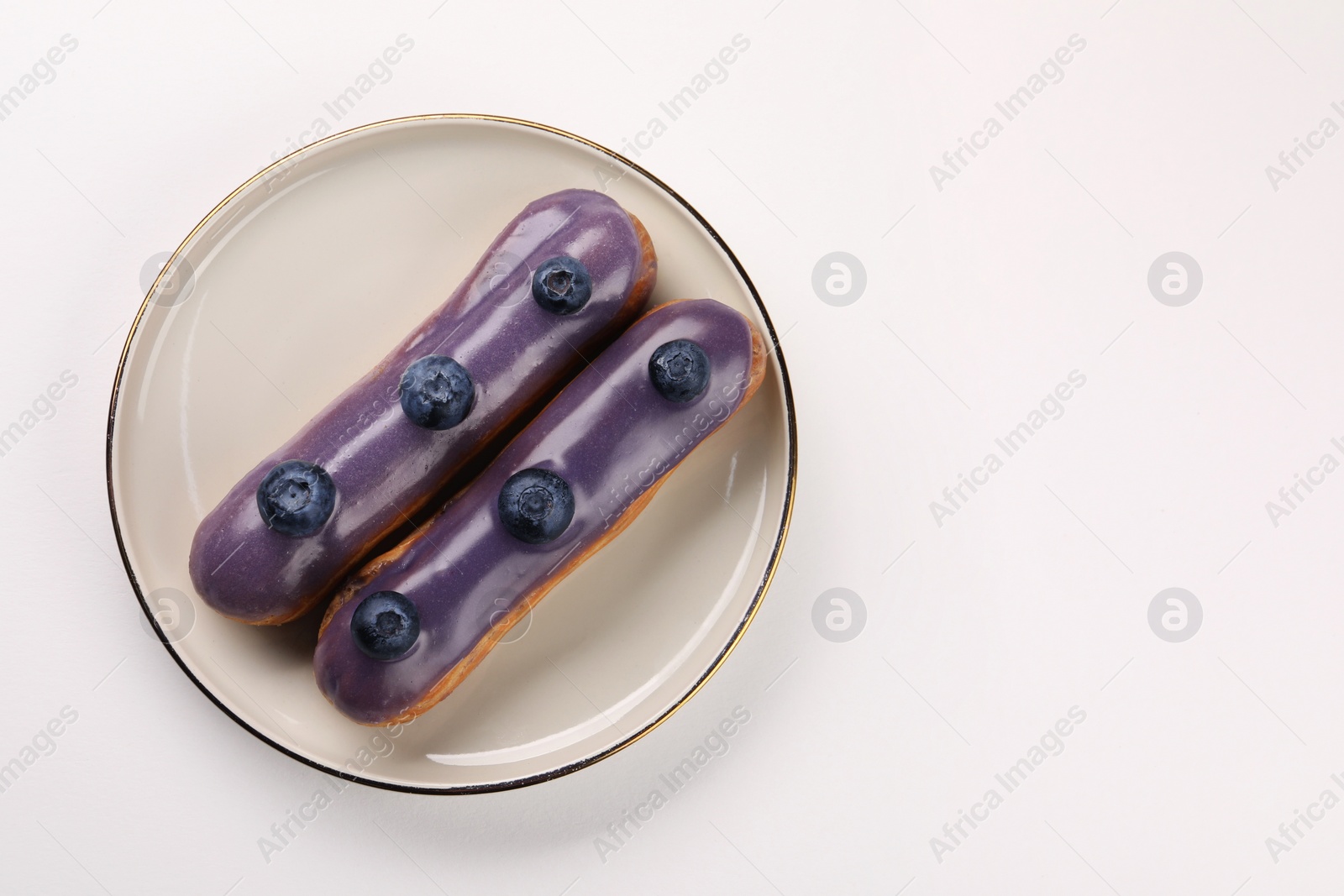 Photo of Delicious eclairs decorated with blueberries on white background, top view