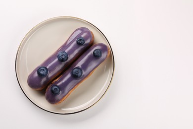 Photo of Delicious eclairs decorated with blueberries on white background, top view