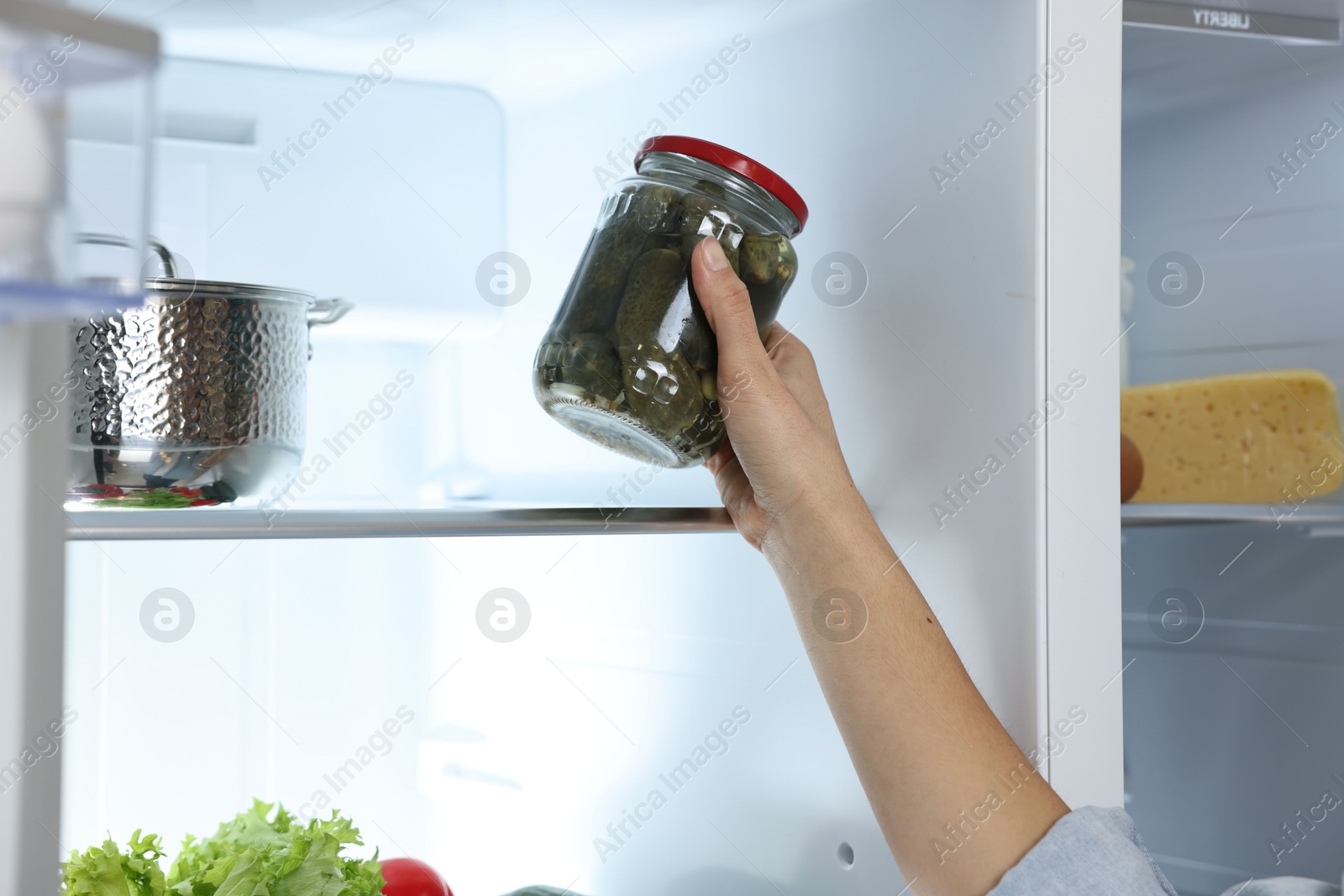 Photo of Young woman taking jar of pickles out of refrigerator, closeup