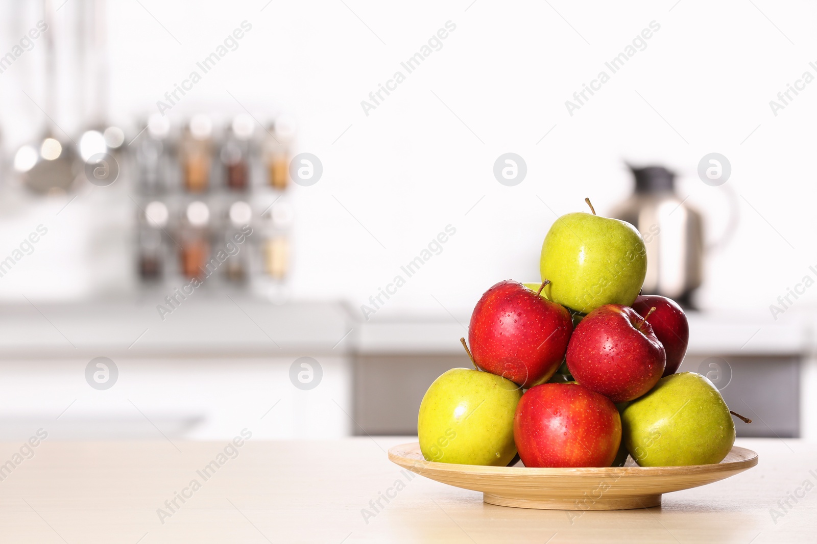 Photo of Plate with different sweet apples on table in kitchen, space for text