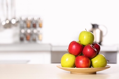 Photo of Plate with different sweet apples on table in kitchen, space for text