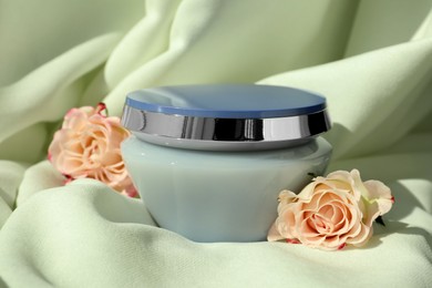 Jar of hair care cosmetic product and beautiful flowers on light green fabric