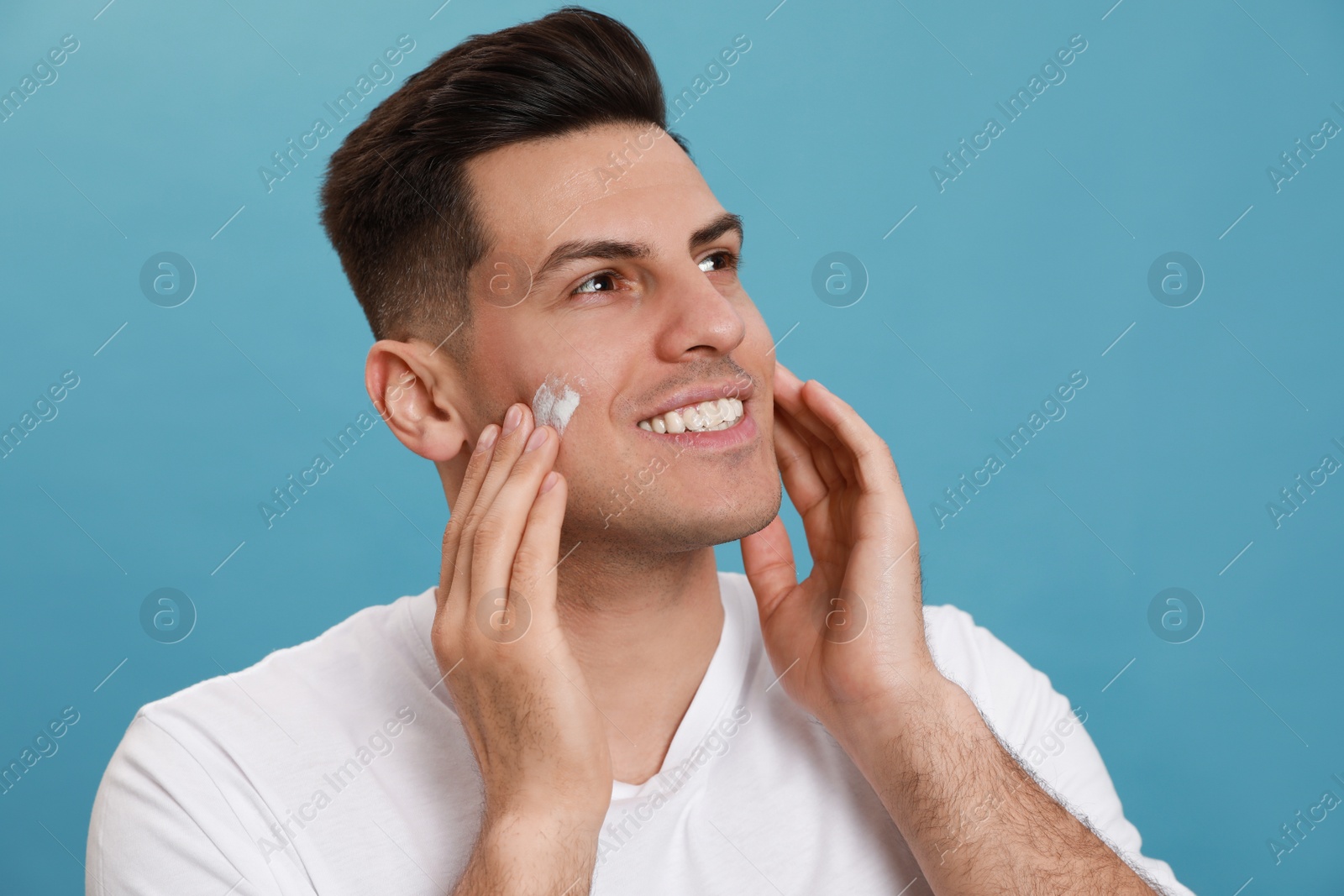 Photo of Happy handsome man applying face cream against turquoise background